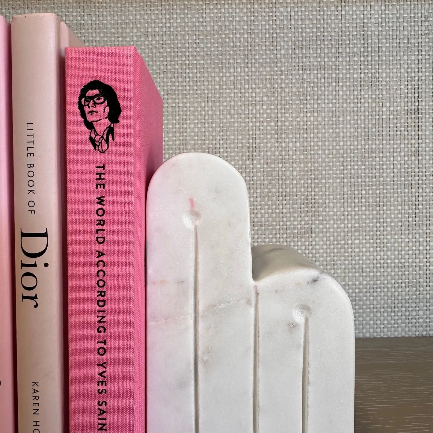 White natural marble curved bookends in retro shape, displaying a selection of pink coffee table books including The Little Book of Valetino, The Little Book of Dior, and The World According to Yves Saint Laurent. All available to purchase at Albury House Interiors.