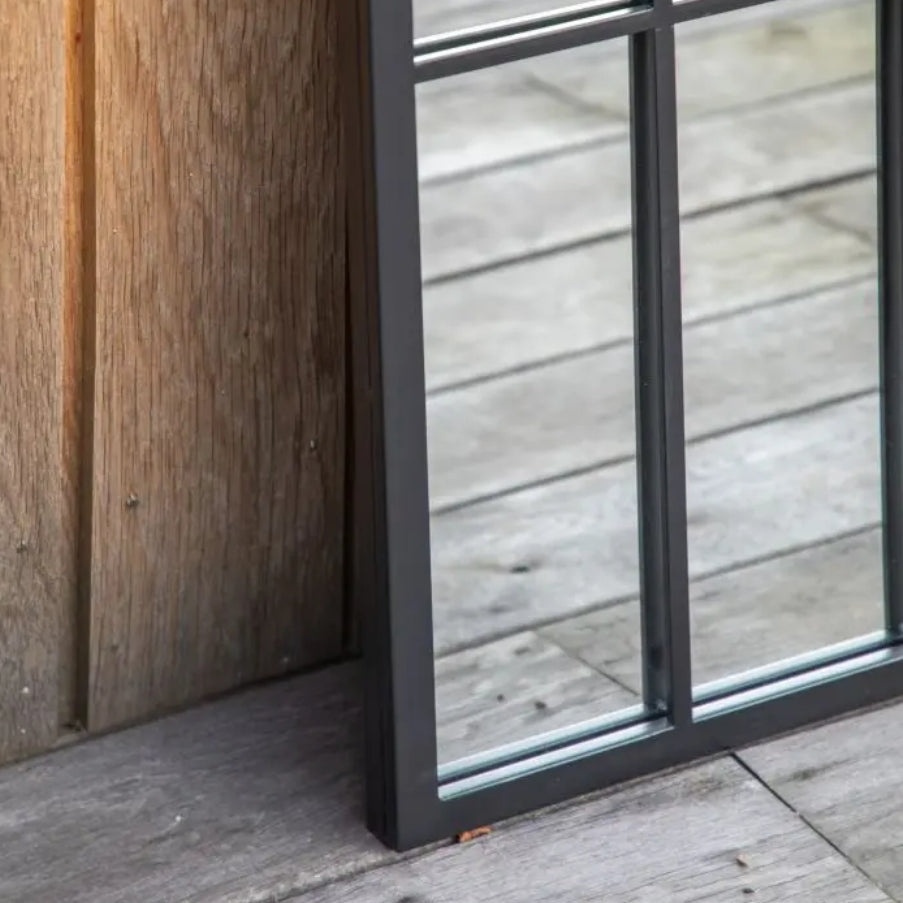 An arched industrial-style mirror with a black metal frame and grid pattern, shown against a desked background. Available at Albury House Interiors