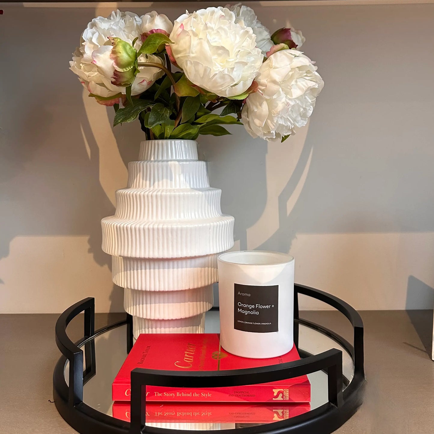 white-ribbed-tier-vase-orange-flower-and-magnolia-candle-and-cartier-coffee-table-book-on-black-cruz-mirror-tray-at-albury-house-interiors
