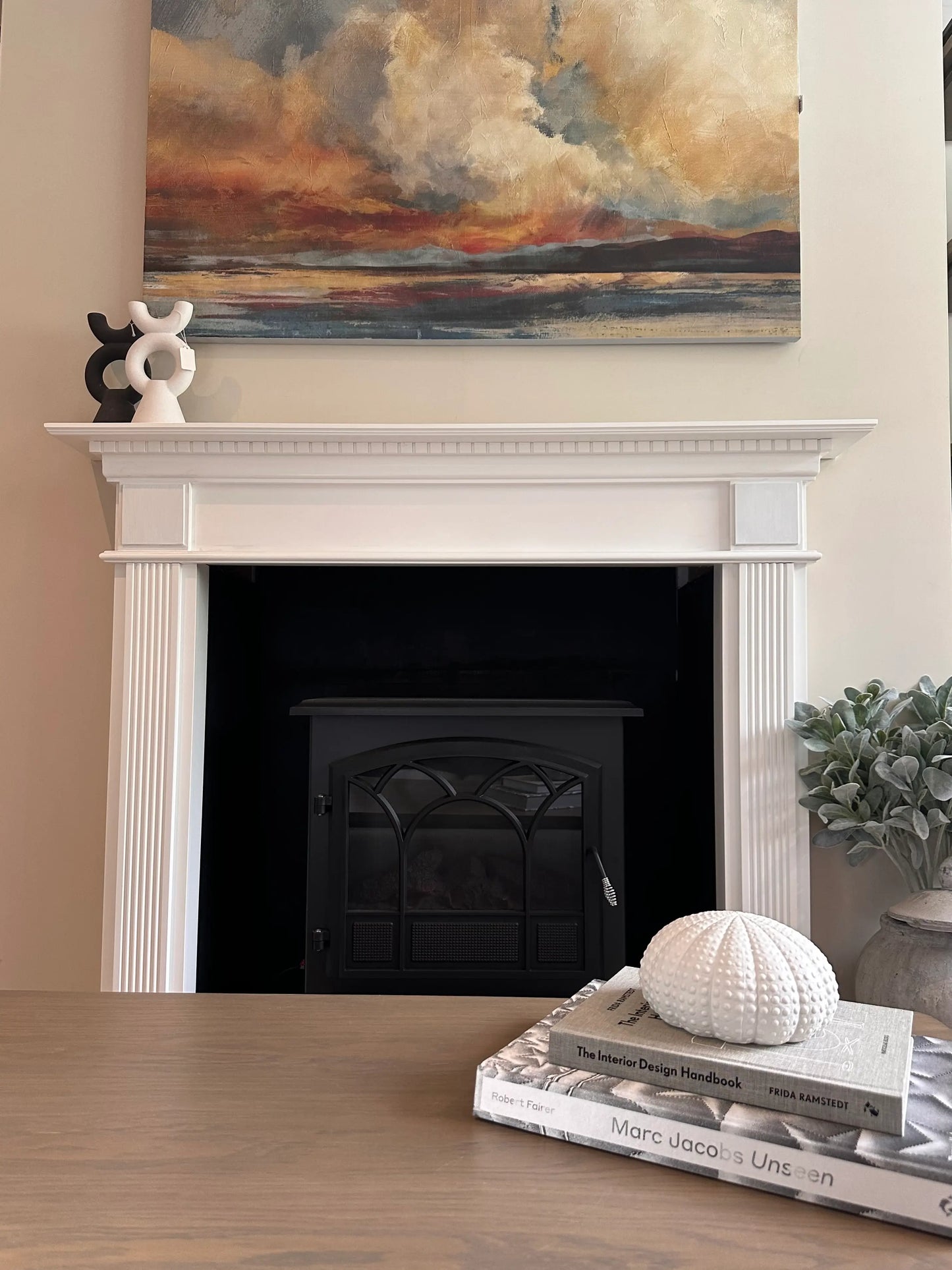white-urchin-ornament-placed-on-stack-of-designer-coffee-table-books-infront-of-fireplace-and-mantle-piece-with-large-sunset-artwork-at-albury-house-interiors