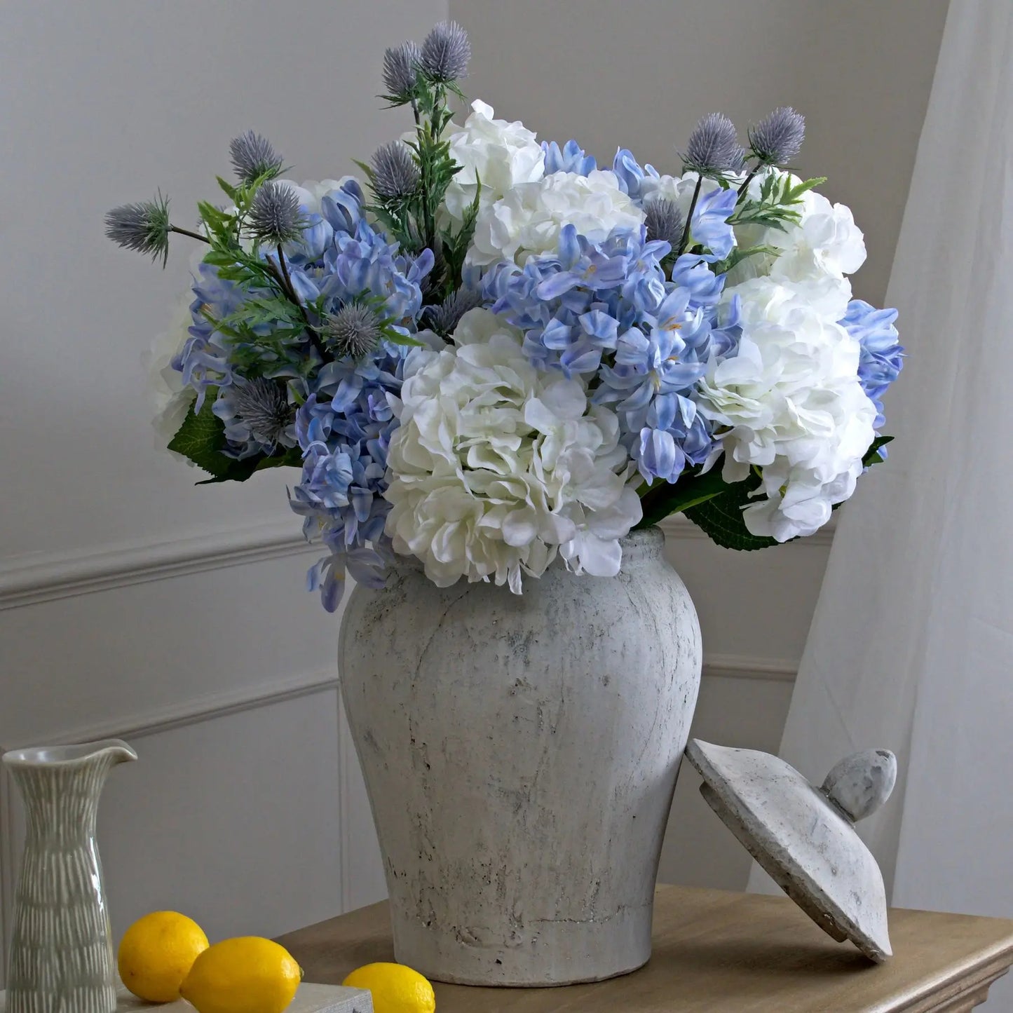 Lidded ginger jar crafted from stone cement and finished in a pale grey with a distressed look, styled with faux white and blue hydrangeas. Available to purchase at Albury House Interiors, homewares in the UK.