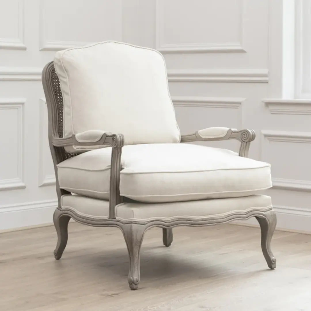 Valais solid oak frame armchair stained in a stone grey with distressed finish. Seat and back cushion upholstered in cream linen with matching armrest padding. Complete with grey rattan back. Available in oak and stone at Albury House Interiors.