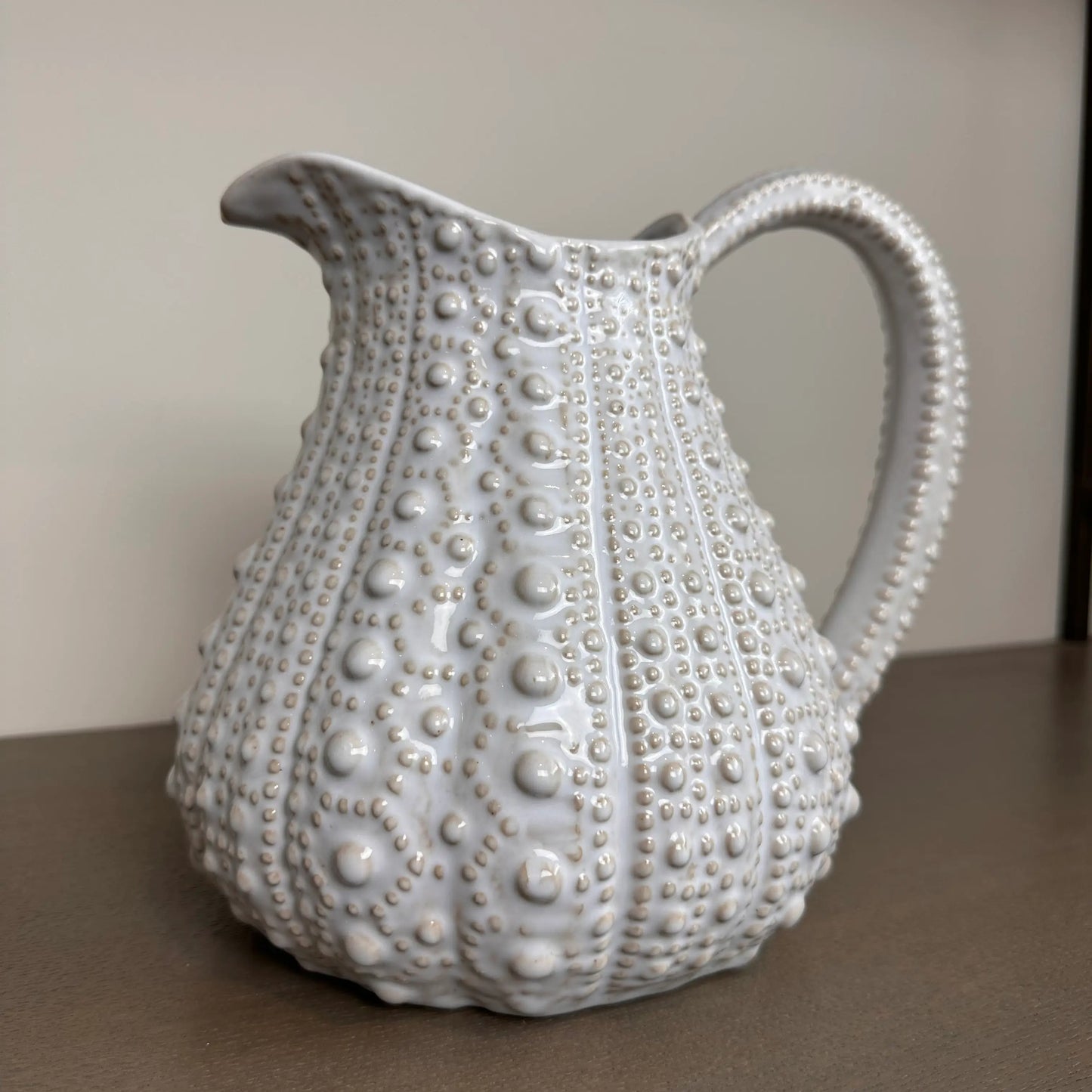 White ceramic urchin jug vase, with dimpled all over texture, large handle and spout. Beautiful in all interiors and rooms due to its versatile colour and shape. Available to purchase at Albury House Interiors, homewares and decor in Essex.