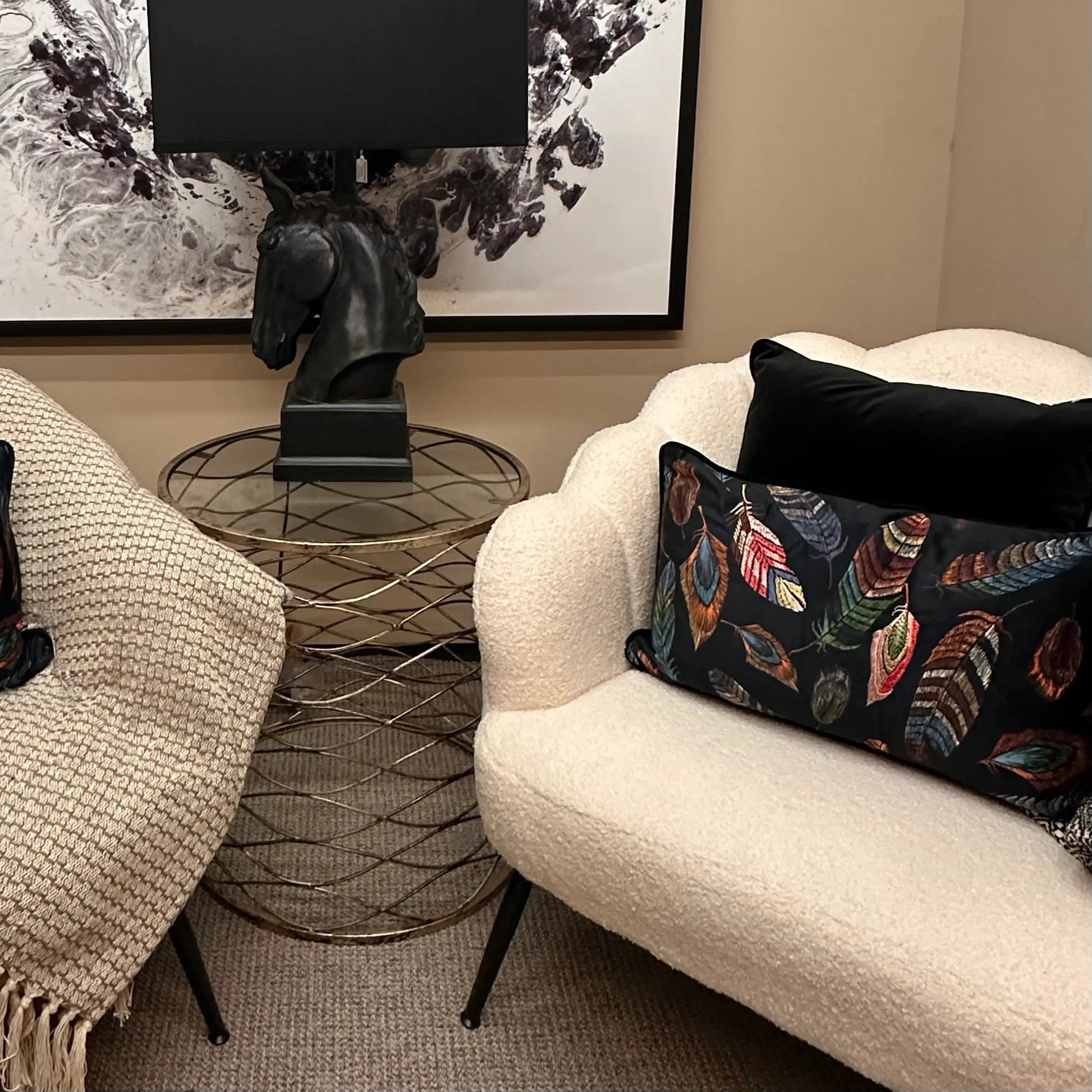 Rectangular shaped black velvet cushion with colourful embroidered feathers and matching black piped edge, complete with feather insert. Paired with plain black velvet cushion and styled on white boucle shell shaped armchair. Available to purchase at Albury House Interiors.