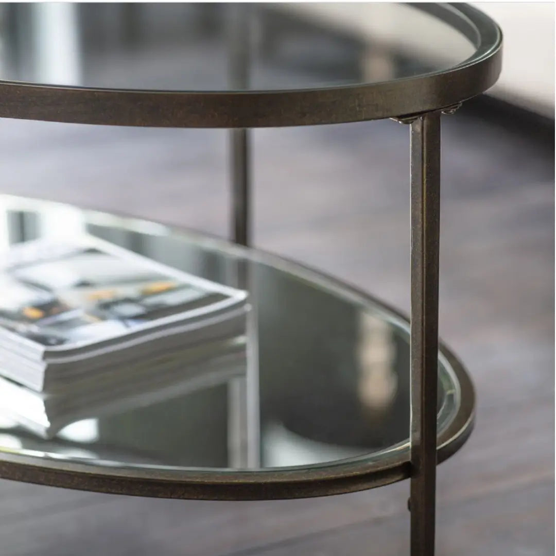 Antique bronze finish curved oval shape coffee table with glass top and mirrored bottom shelf, available at Albury House Interiors.