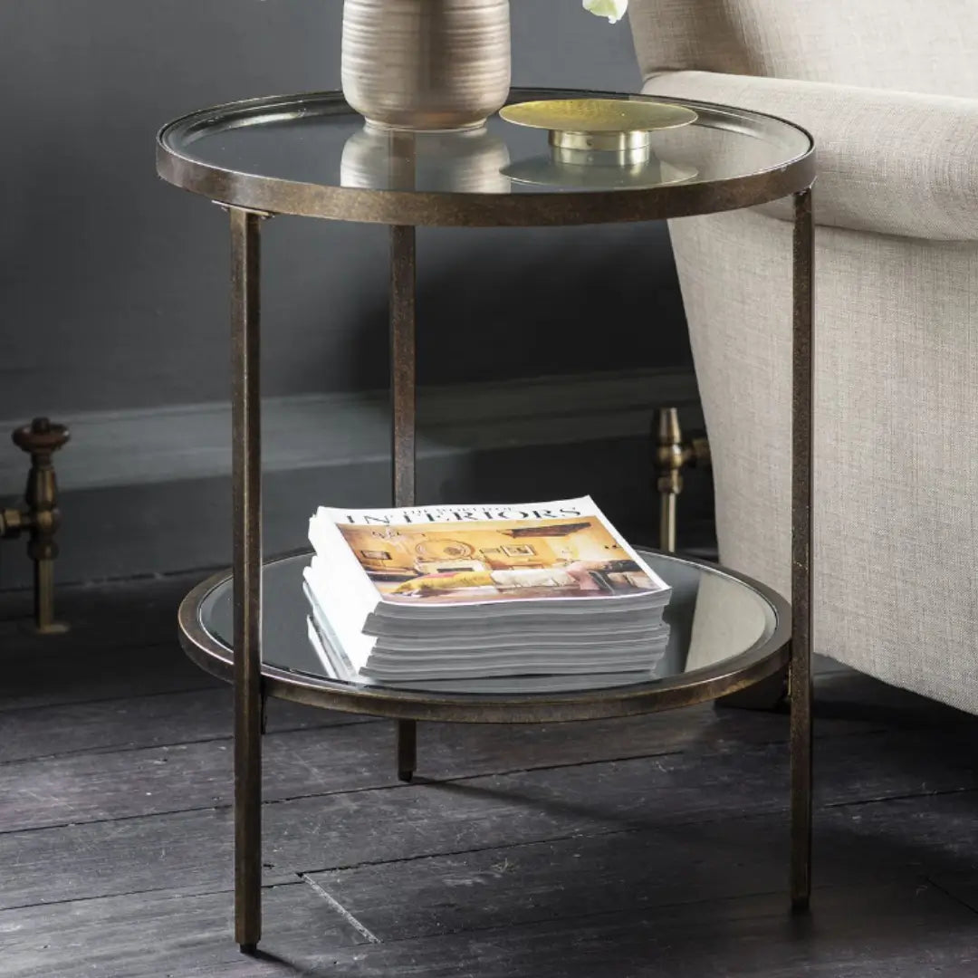 Antique bronze round side table with glass top and mirrored shelf. Perfect for use in bedrooms, living rooms, dining rooms and hallways. Available to purchase from Albury House Interiors, homewares and free standing furniture in the UK.