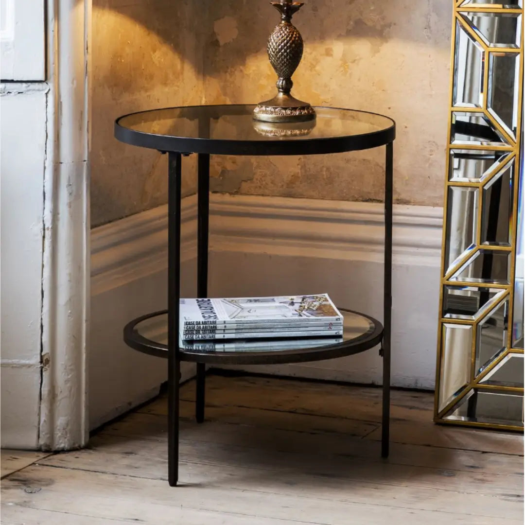 Antique bronze round side table with glass top and mirrored shelf. Perfect for use in bedrooms, living rooms, dining rooms and hallways. Available to purchase from Albury House Interiors, homewares and free standing furniture in the UK.