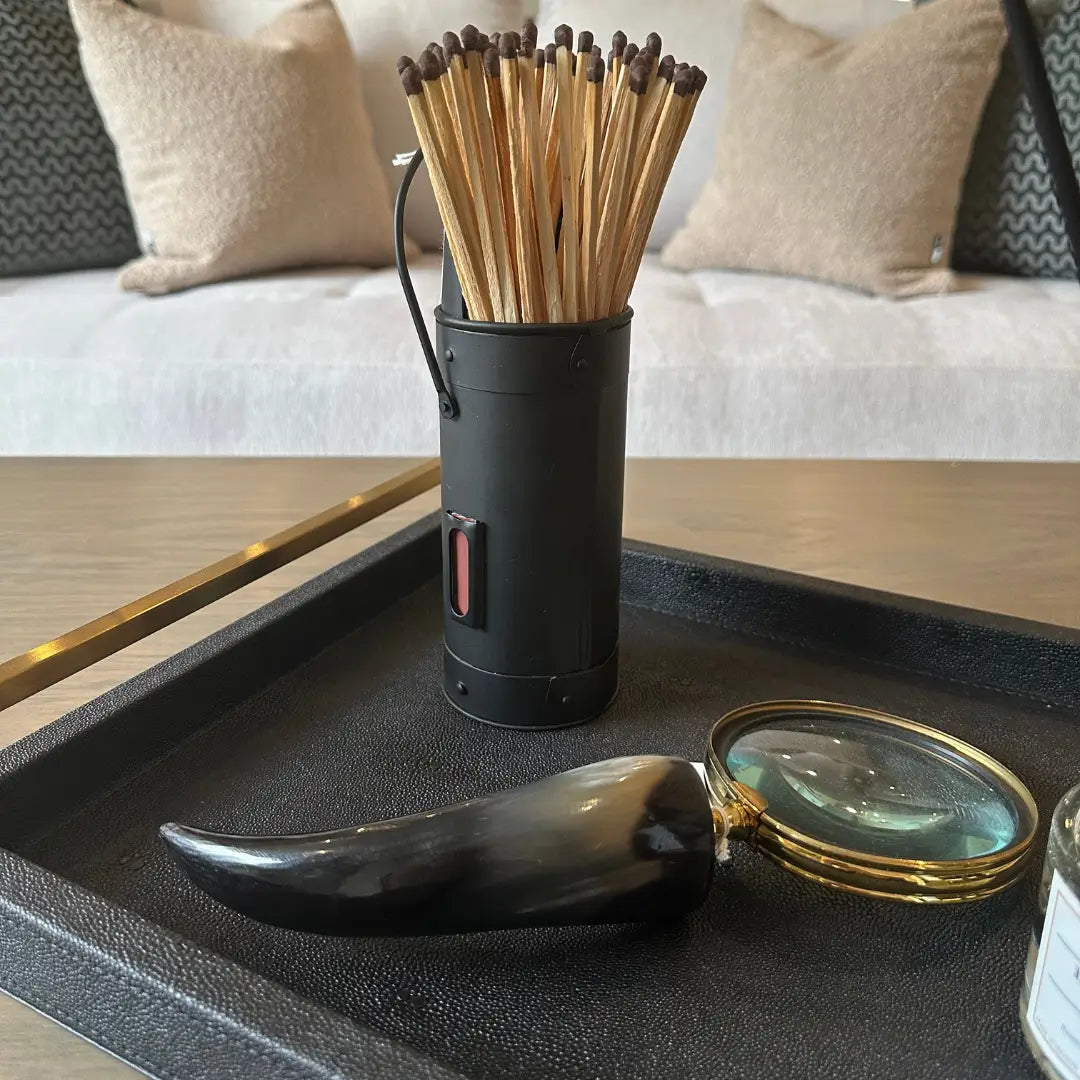 Black steel matchstick holder with faux horn magnifying glass displayed on black shagreen tray with gold handles, all available to purchase at Albury House Interiors.