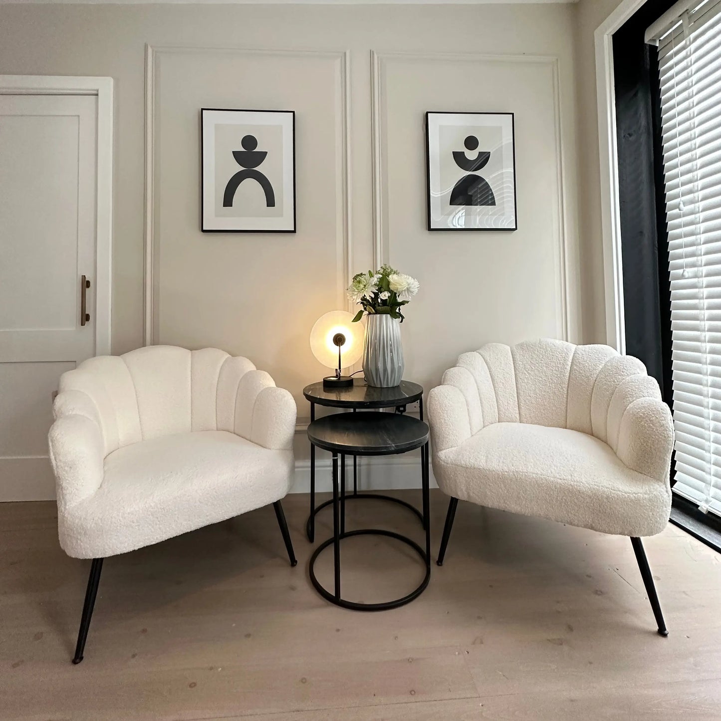 White soft boucle armchair occasion chair in a shell shape with scalloped edges and matte black legs, paired with nesting black marble side tables, black and white abstract artwork and marble lamp. All items available to purchase from Albury House Interiors, Essex. 