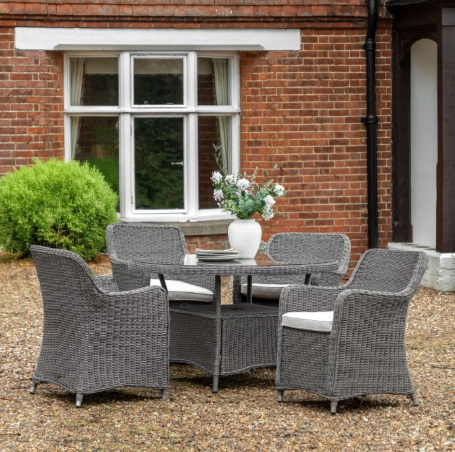 A 5-piece outdoor dining set featuring a round glass-top table and four high-back grey woven wicker chairs with white seat cushions, shown against a plain white background available at Albury House Interiors.