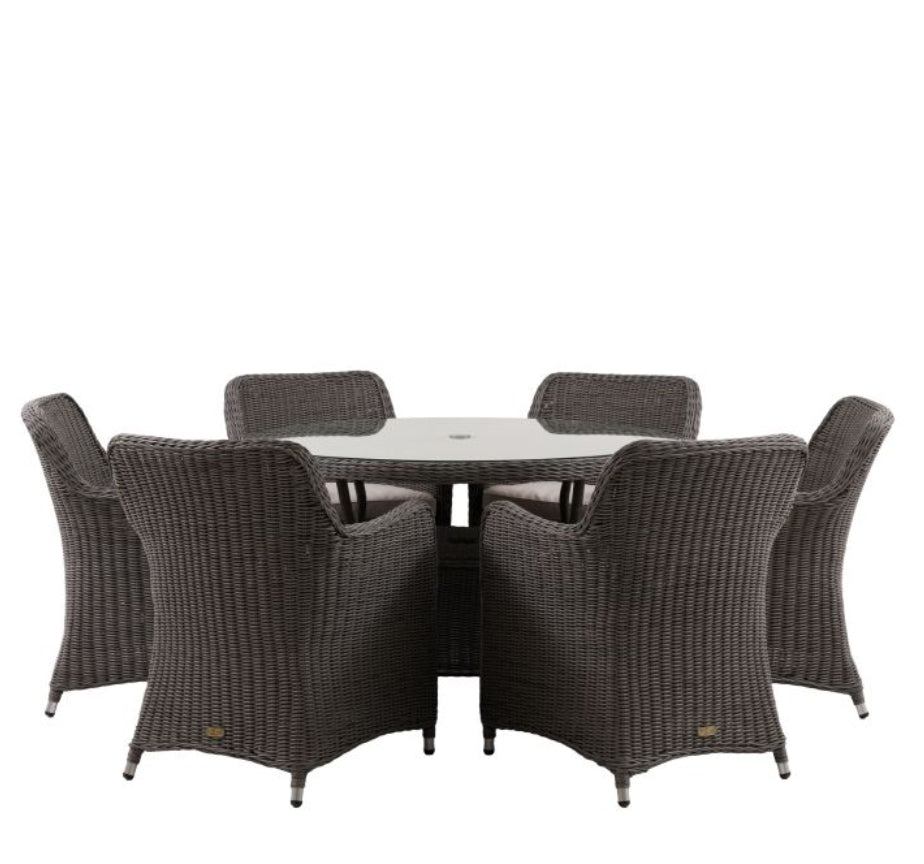A 7-piece outdoor dining set featuring a round glass-top table and six grey woven wicker armchairs, shown against a plain white background. Available at Albury House Interiors.
