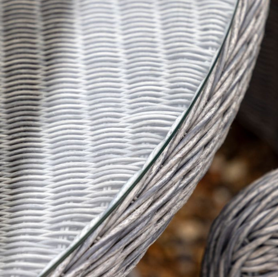 A 7-piece outdoor dining set featuring a round glass-top table and six grey woven wicker armchairs, shown against a plain white background. Available at Albury House Interiors.
