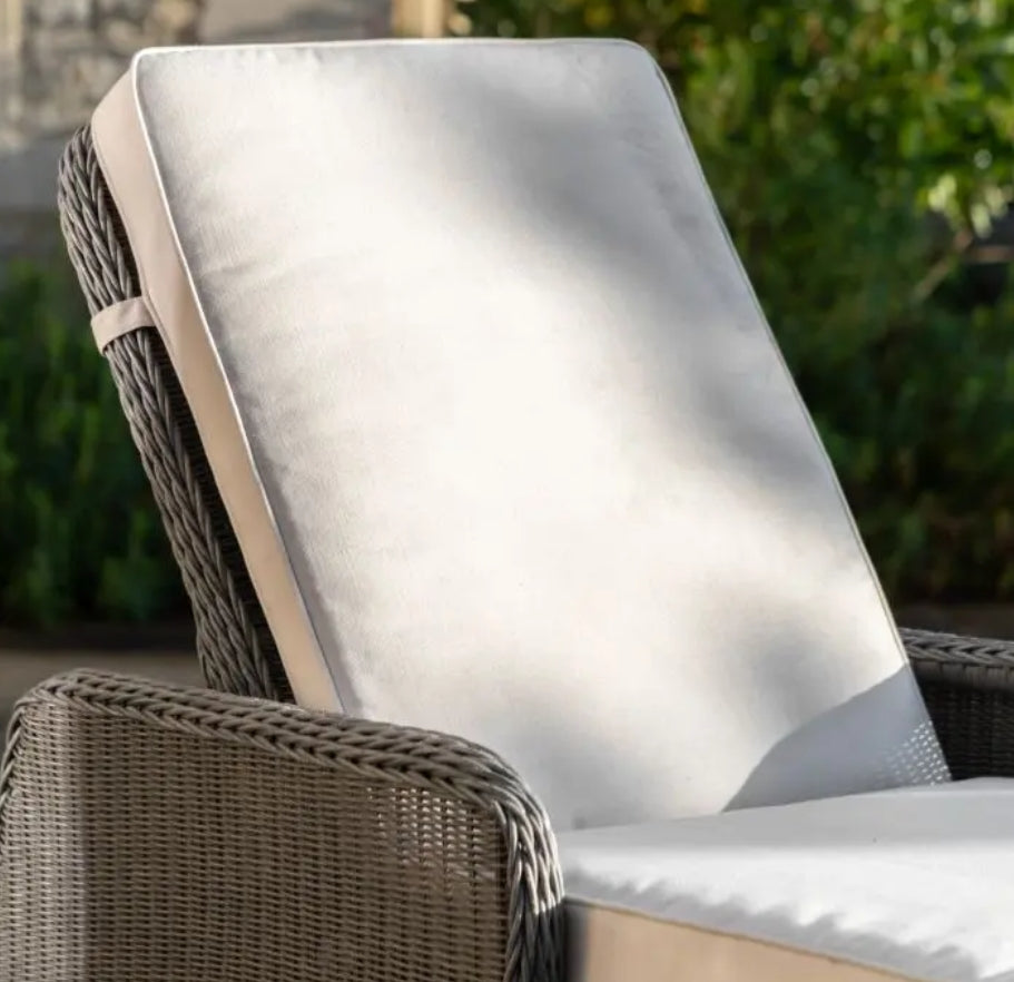 An outdoor reclining wicker Lounger with a tall backrest, featuring light beige cushions on the seat and back, set against a plain white background.