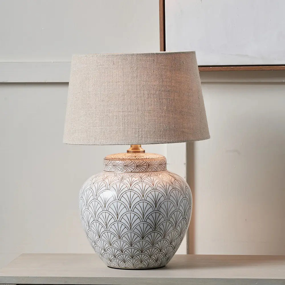 white-ceramic-lamp-base-with-art-deco-fan-repeating-pattern-and-brass-detailing-with-neutral-linen-lampshade-at-albury-house-interiors