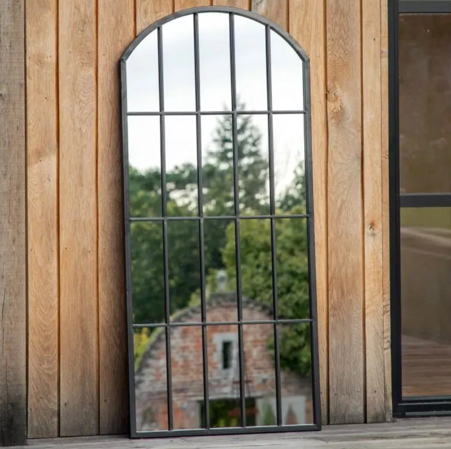 An arched industrial-style mirror with a black metal frame and grid pattern, shown against a plain white background. Available at Albury House Interiors