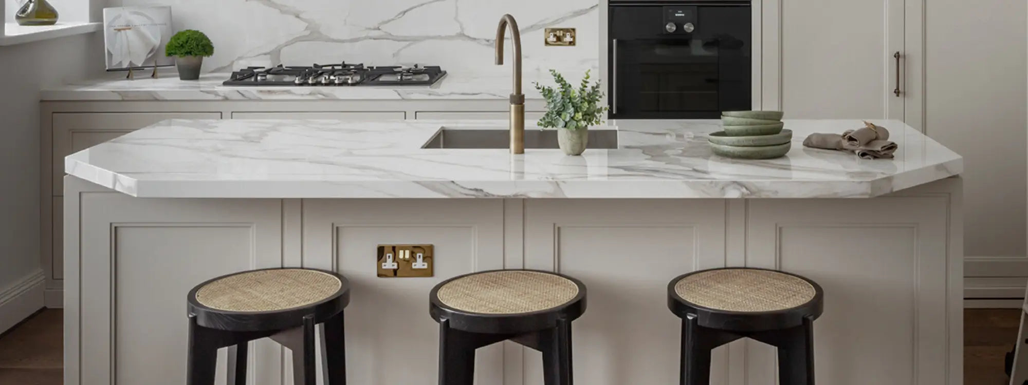 bespoke-kitchen-with-natural-white-and-grey-marble-island-black-and-rattan-kitchen-stools-and-antique-brass-tap-designed-by-interior-designers-cochrane-design-manufactured-by-chordal-green-ltd-essex-london