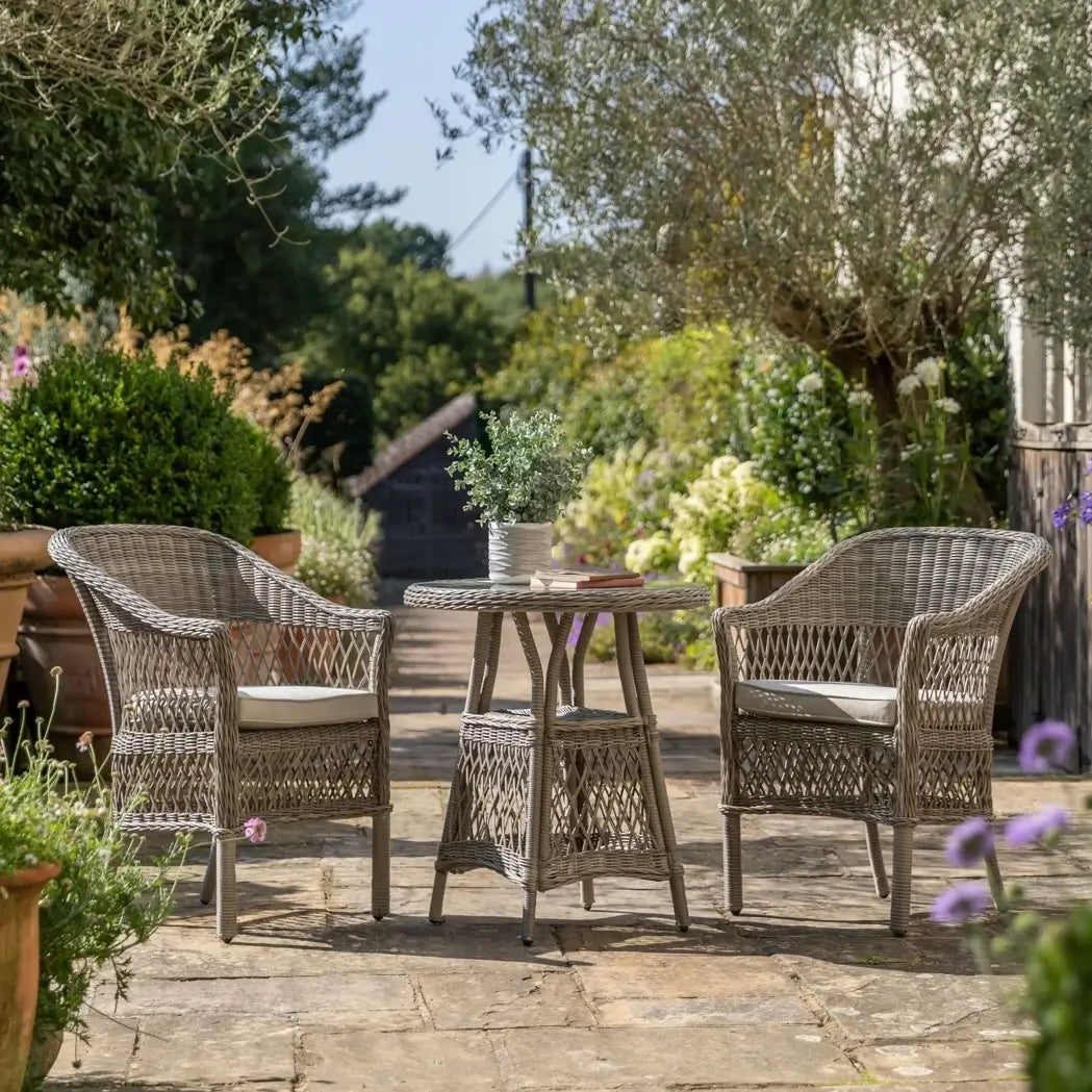 Moreton rattan woven outdoor bistro set with two armchair style seats with natural coloured weatherproof cushions and round rattan glass top table. Available to purchase at Albury House Interiors.