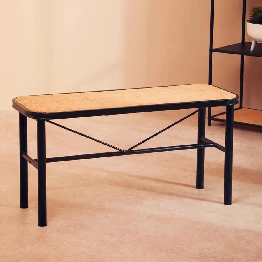 Natural rattan seated bench supported by a black metal frame with tubular legs and a V frame. Available to purchase from Albury House Interiors, Matching Tye Essex. 