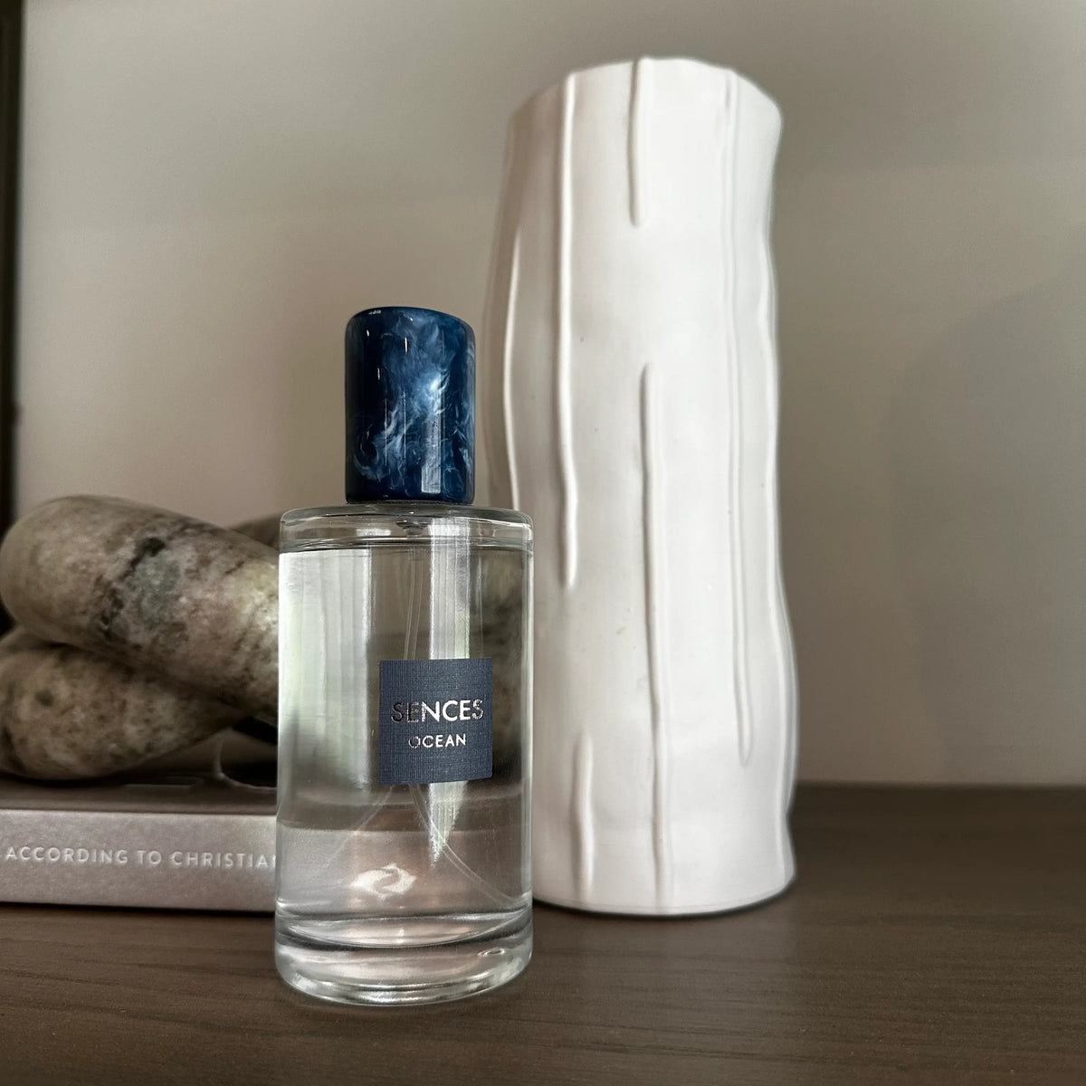 Glass bottle of Sences Ocean room spray with a dark blue marbled cap stands next to its blue packaging box. Perfect for giving. Available to purchase from Albury House Interiors.
