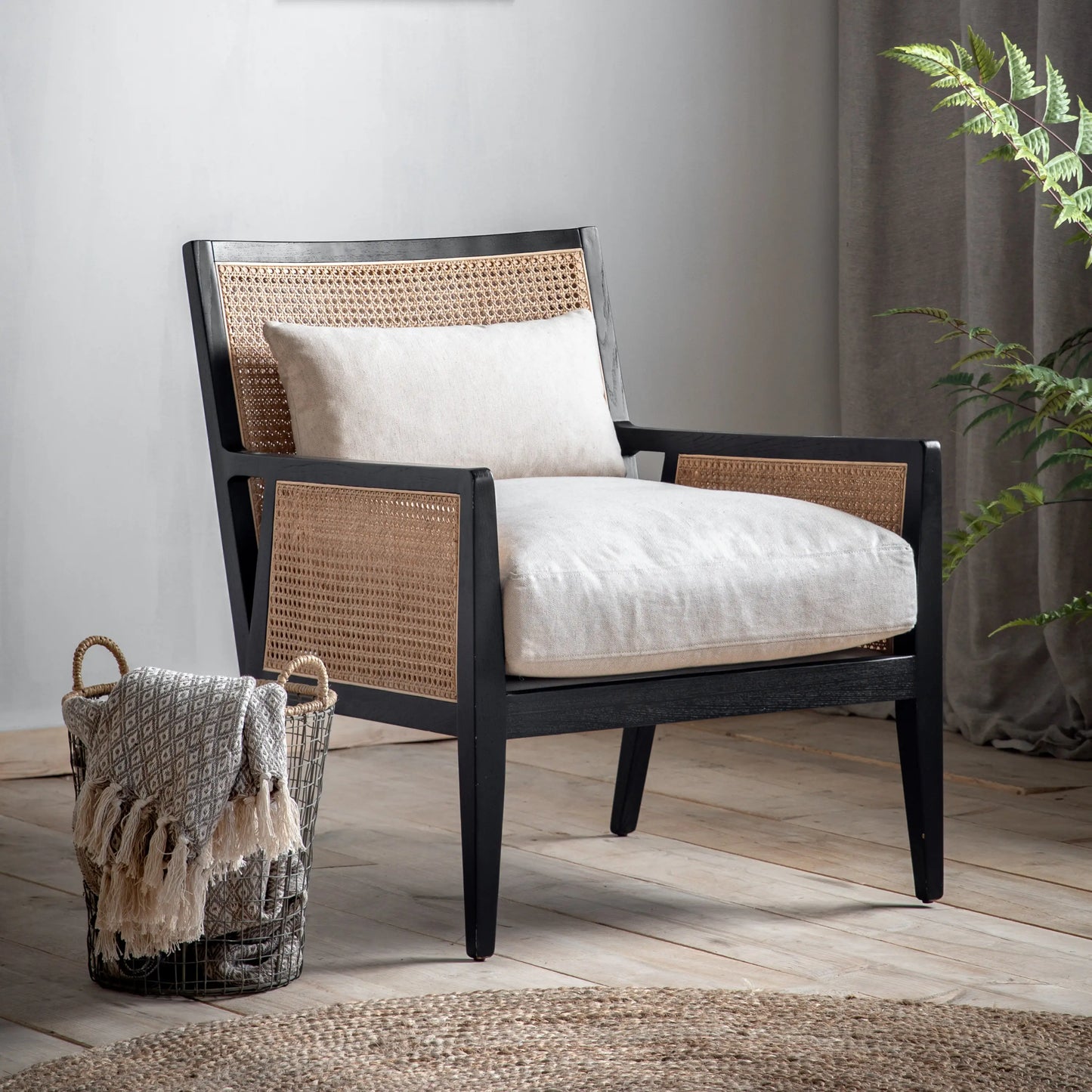 Rattan armchair with black wooden frame and natural coloured rattan, includes a neutral seat cushion and back cushion. Available at Albury House Interiors Essex.