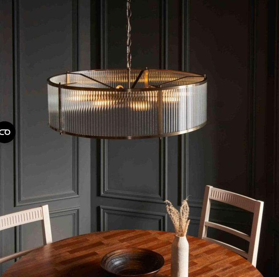 Ribbed glass, brass finish circular Chandelier light hanging above a wooden table with chairs in a room with dark paneled walls.