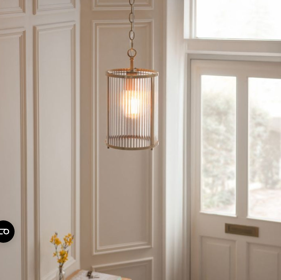 Pendant brass metal light with ribbed glass shade hung on a chain, in a hallway
