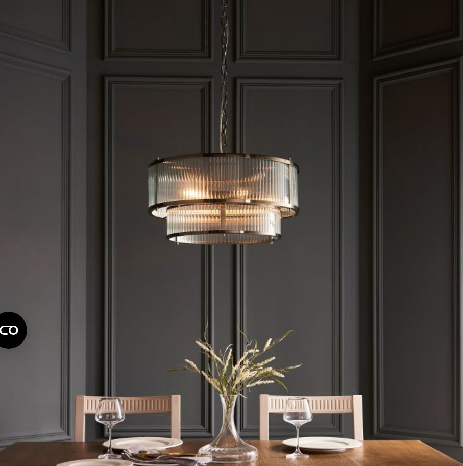 A two-tier drum pendant chandelier light with a brushed brass frame and clear ribbed glass panels, suspended from a matching chain against a white background, available from Albury House Interiors.