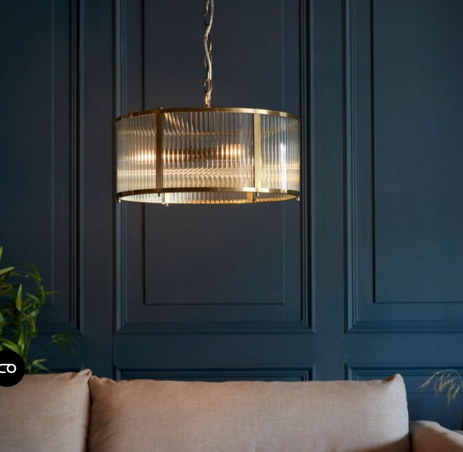 Chandelier with brass finish and clear, ribbed, glass shade hung on a metal chain, in front of a navy panelled wall