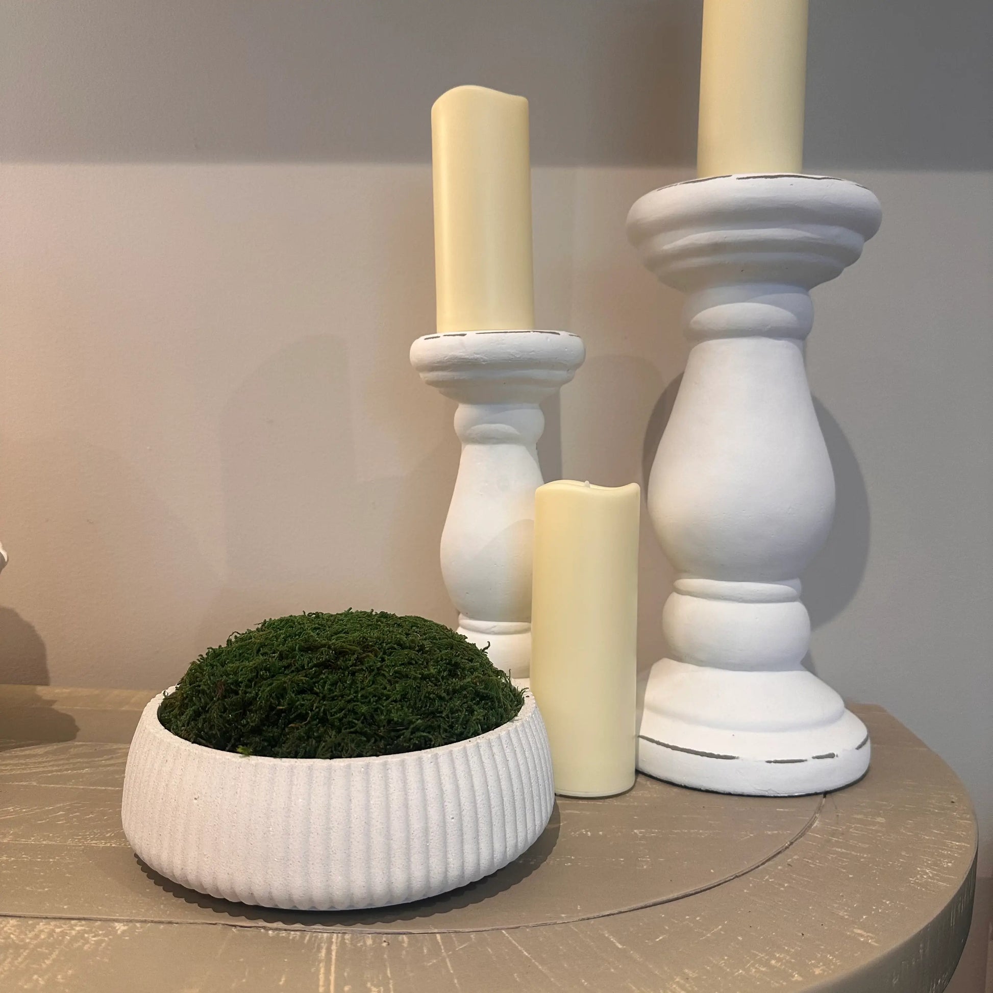 Ribbed white mineral jesmonite stone preserved green moss bowl, used by interior designers, alongside white ceramic oversized candle holders. Available to purchase at Albury House Interiors.