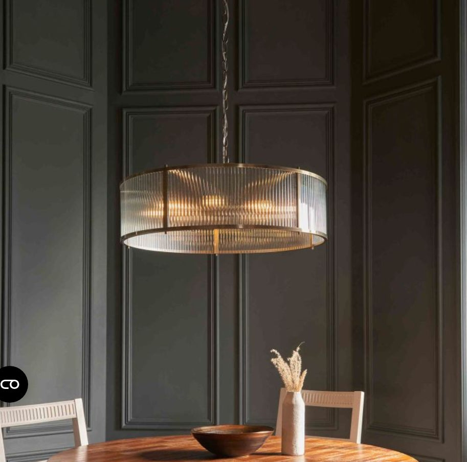 Ribbed glass, brass finish circular Chandelier light hanging above a wooden table with chairs in a room with dark panelled walls.