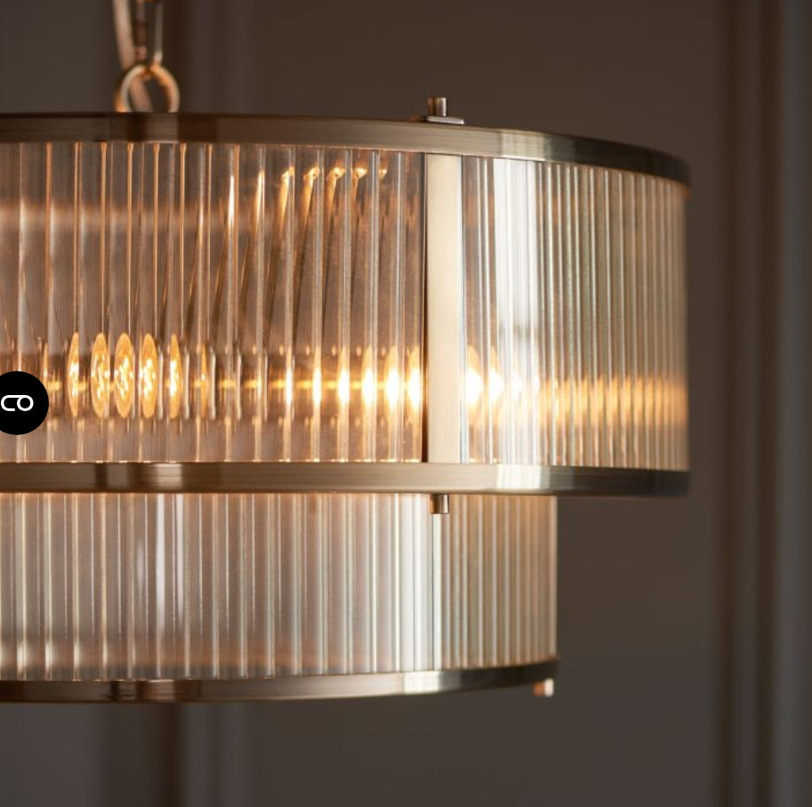 A two-tier drum pendant chandelier light with a brushed brass frame and clear ribbed glass panels, suspended from a matching chain against a white background, available from Albury House Interiors.