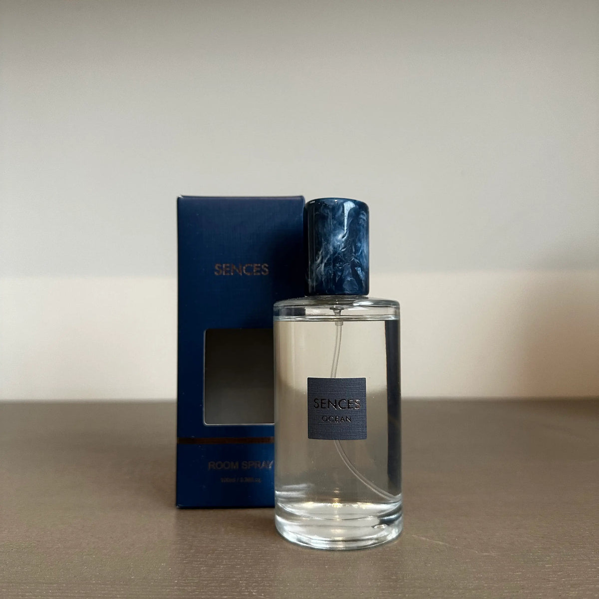 Glass bottle of Sences Ocean room spray with a dark blue marbled cap stands next to its blue packaging box. Perfect for giving. Available to purchase from Albury House Interiors.