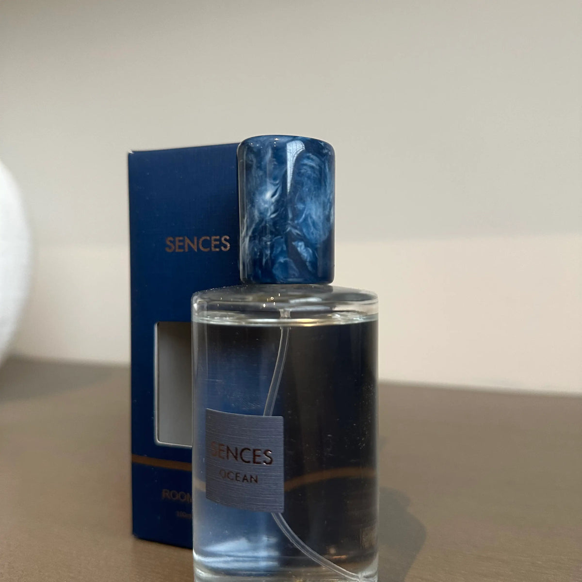 Glass bottle of Sences Ocean room spray with a dark blue marbled cap stands next to its blue packaging box. Perfect for giving. Available to purchase from Albury House Interiors.