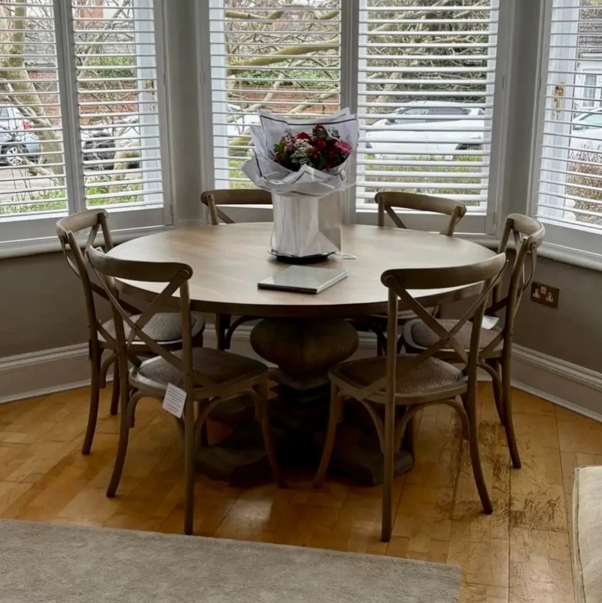 Wardour round solid wood dining table with intricate detail base and six matching wooden dining chairs, in bay window of dining room. Available to purchase at Albury House Interiors.