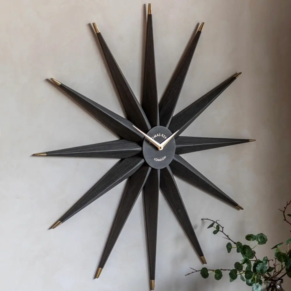 Starburst statement wall clock in North Star shape crafted from wood and finished in a dark warm grey, with gold accents and matching clock hands. Available to purchase from Albury House Interiors, home decor and accessories shop in Essex. 