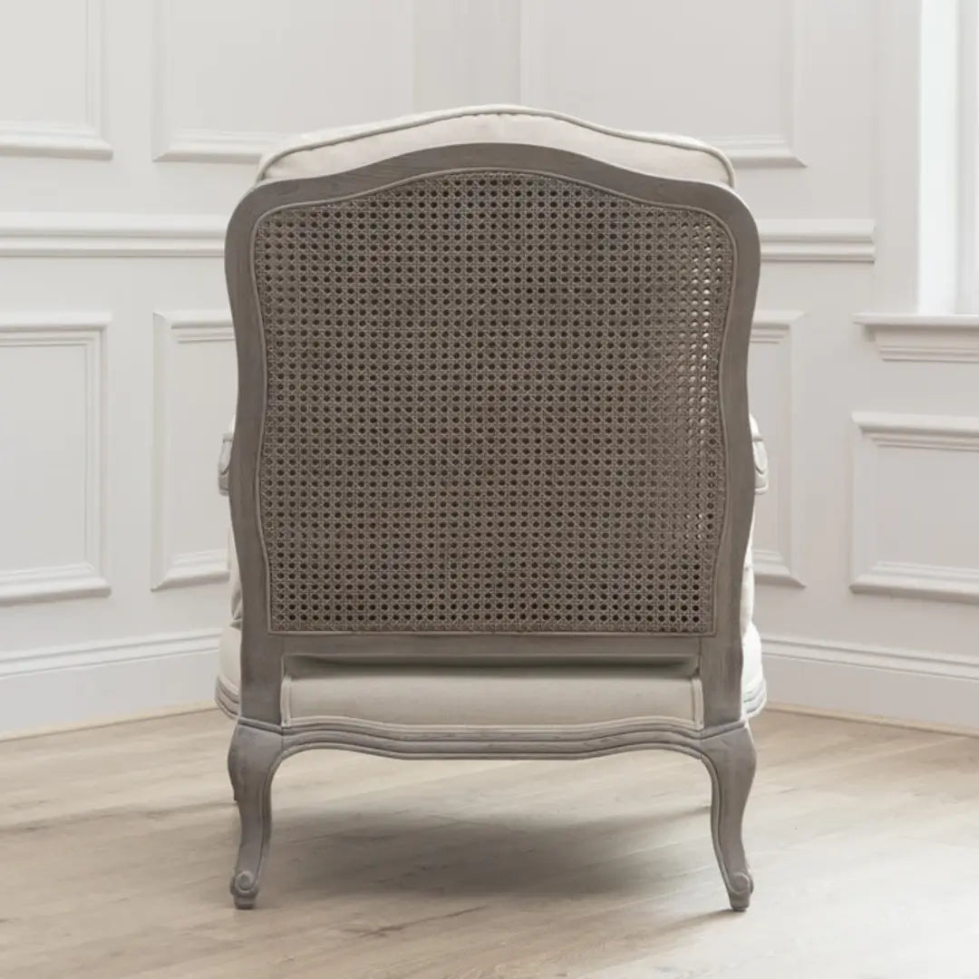 Valais solid oak frame armchair stained in a stone grey with distressed finish. Seat and back cushion upholstered in cream linen with matching armrest padding. Complete with grey rattan back. Available in oak and stone at Albury House Interiors.